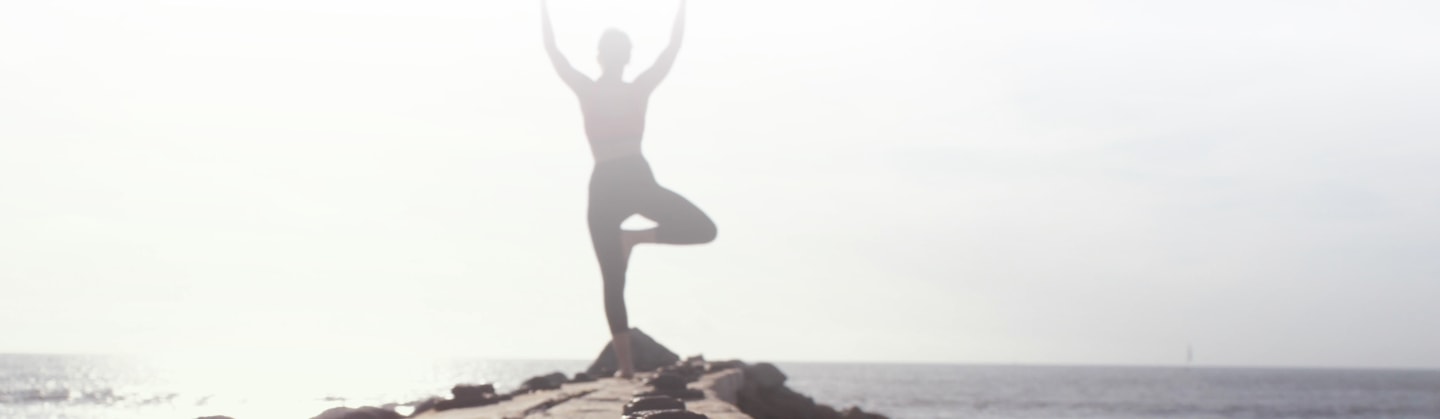 Person doing yoga on a rock near the water